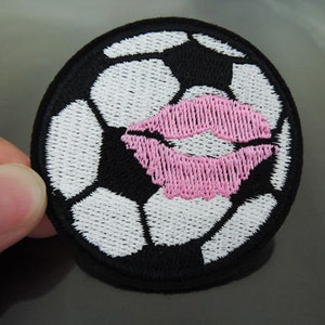 Könnte beinhalten: Schwarzer und weißer gestickter Fußball-Patch mit einem gestickten rosa Lippen-Design.