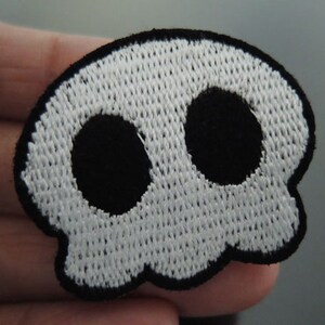 Könnte beinhalten: Weißer gestickter Totenkopf-Patch mit schwarzen Augenhöhlen.