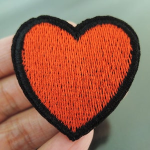 May include: A red heart-shaped embroidered patch with a black outline.