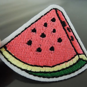May include: A red and green embroidered watermelon patch with black seeds. The patch is on a white background.