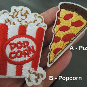 May include: Two embroidered iron-on patches, one of a slice of pizza with red pepperoni and the other of a red and white striped popcorn bucket with popcorn on top. The text "A - Pizza" and "B - Popcorn" are below the patches.