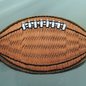 May include: Brown leather football with white stitching. The football is embroidered with a detailed design.