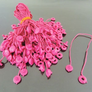 May include: A pile of pink string with plastic loops at the end. The string is tied together with a yellow rubber band.
