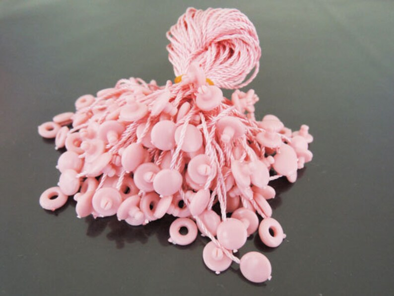May include: A bunch of pink string with plastic buttons at the end. The string is tied together in a bundle.
