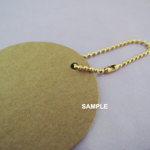 May include: A round, brown paper tag with a gold chain attached. The tag has the word "SAMPLE" printed on it.