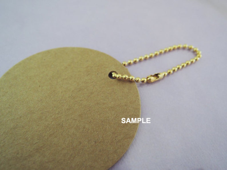 May include: A round, brown paper tag with a gold chain attached. The tag has the word "SAMPLE" printed on it.