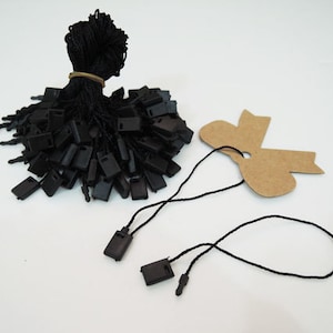 May include: A pile of black plastic tags with black string attached. The tags are in the shape of a rectangle with a hole in the center. There are two separate strings with tags attached, one of which is looped.
