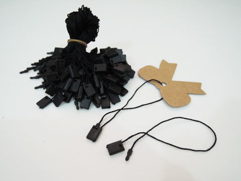 May include: A pile of black plastic tags with black string attached. The tags are in the shape of a rectangle with a hole in the center. There are two separate strings with tags attached, one of which is looped.