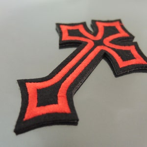 Peut inclure: Patch brodé en forme de croix noire et rouge. La croix est bordée de rouge et a un centre noir.