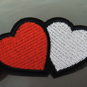 May include: Two embroidered hearts, one red and one white, sewn together. The hearts are outlined in black.