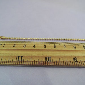 May include: A gold ball chain measuring 9 inches long. The chain is laid out on a wooden ruler.