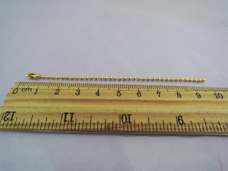 May include: A gold ball chain measuring 9 inches long. The chain is laid out on a wooden ruler.