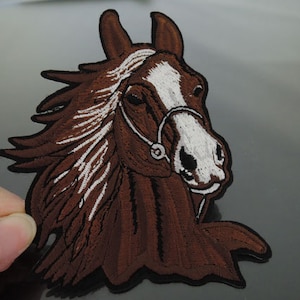 May include: Brown and white embroidered horse head patch with a black border. The horse has a white bridle and a brown mane and tail.