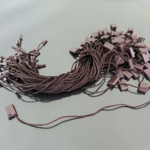 May include: A pile of brown string with brown plastic tags attached. The tags have a small hole in the top for threading the string.