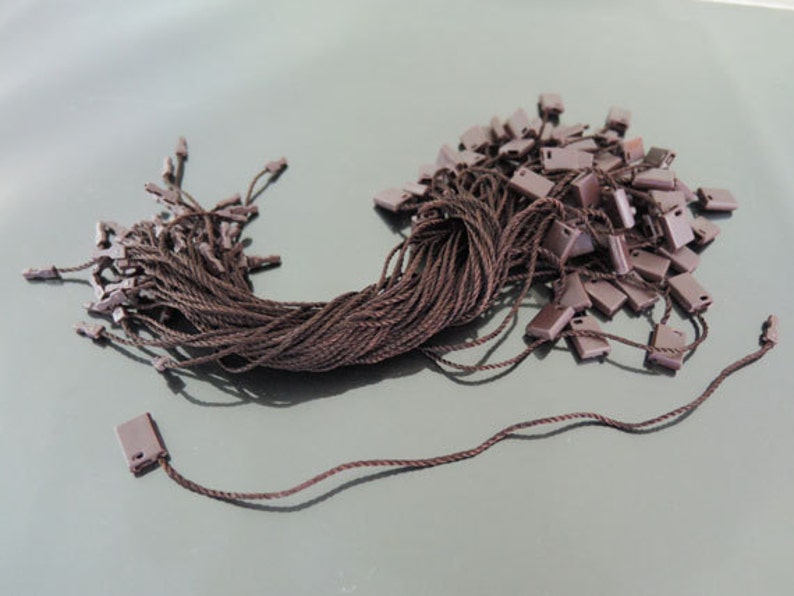 May include: A pile of brown string with brown plastic tags attached. The tags have a small hole in the top for threading the string.