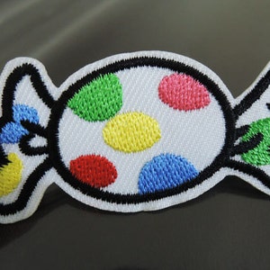 May include: A white candy-shaped patch with a black outline and colorful polka dots. The dots are red, yellow, green, and blue.