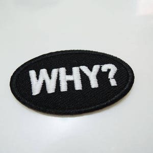 May include: Black oval patch with white embroidered text that reads "WHY?"