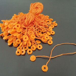 以下が含まれることがあります： オレンジ色の紐の大きな束に、小さなオレンジ色のプラスチック製のループが取り付けられています。紐は束ねられています。