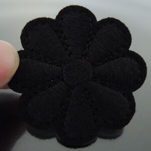 Könnte beinhalten: Schwarze Filzblumenapplikation mit gewelltem Rand. Die Blume hat ein einfaches Design mit fünf Blütenblättern.
