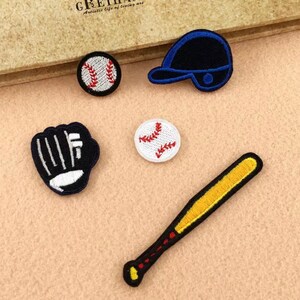 Könnte beinhalten: Fünf gestickte Bügelbilder mit Baseball-Ausrüstung: ein Baseball, ein Baseballschläger, ein Baseballhandschuh, eine Baseballkappe und ein zweiter Baseball.