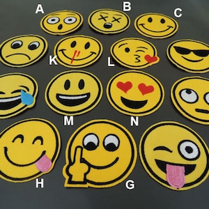 May include: A collection of yellow emoji patches with various expressions, including smiling, winking, and crying. Each patch has a black border and is made of fabric. The patches are round and vary in size.
