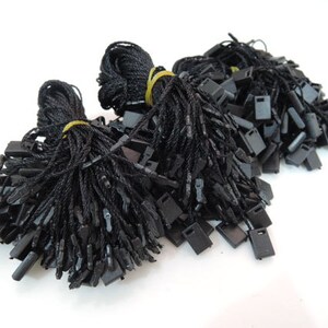 May include: A bulk pack of black string tags with black plastic tips. The tags are bundled together and ready to be used for labeling or attaching to items.
