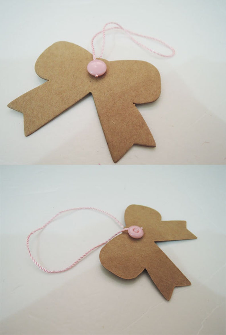 May include: A brown paper bow with a pink button in the center. The bow is attached to a pink and white string.