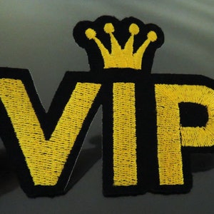 Könnte beinhalten: Gestickter Aufnäher mit den Buchstaben "VIP" in gelbem Faden auf schwarzem Grund, gekrönt von einer gelben Krone. Der Aufnäher ist zum Aufnähen oder Aufbügeln auf Kleidung oder Accessoires gedacht.