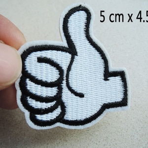 May include: White embroidered thumbs up patch with a black outline. The patch is 5 cm by 4.5 cm.
