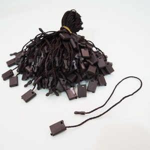 May include: A pile of brown string tags with black plastic loops. The tags are used for attaching price tags or other information to products.