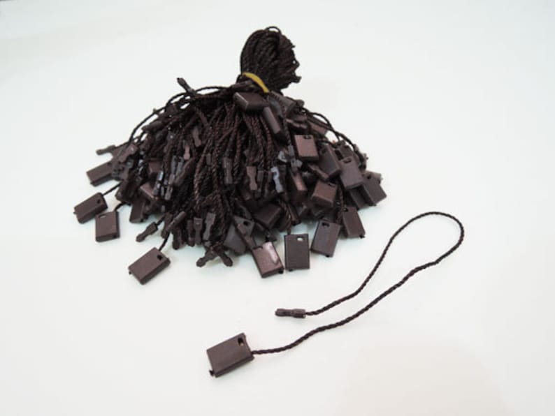 May include: A pile of brown string tags with black plastic loops. The tags are used for attaching price tags or other information to products.