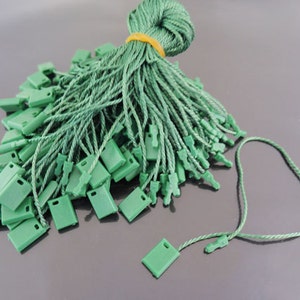 以下が含まれることがあります： プラスチック製の先端が付いた緑色の紐タグのバルクパック。タグは束ねられており、ラベル付けやアイテムへの取り付けに使用できます。