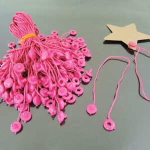 May include: A bundle of pink string with plastic tags, and a separate pink string with a brown star-shaped tag.