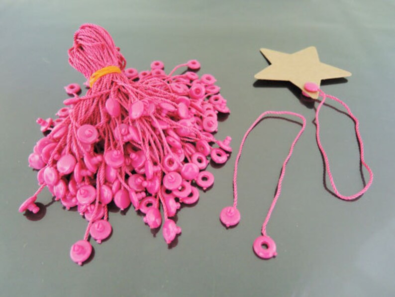 May include: A bundle of pink string with plastic tags, and a separate pink string with a brown star-shaped tag.