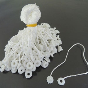 May include: A bunch of white string tags with a white plastic ring and a white plastic button at the end of each string.
