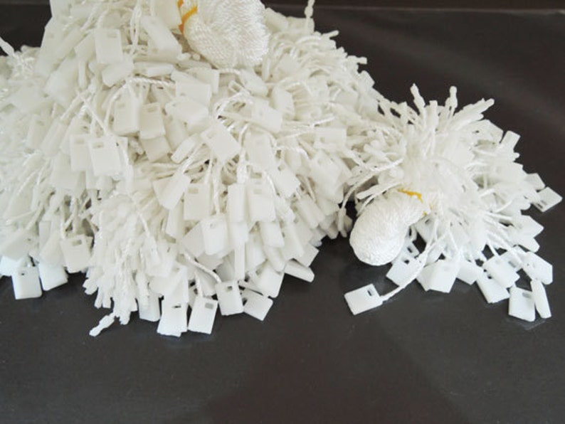 May include: A large pile of white plastic tags with strings attached. The tags are rectangular with a small hole in the top. The strings are white and are tied together in a knot at the top.