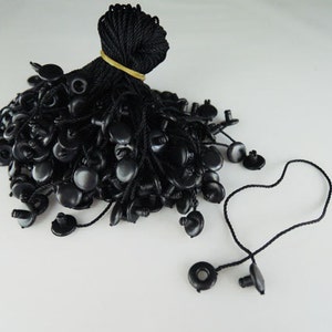 以下が含まれることがあります： 黒いプラスチック製のコードエンドの束で、各端に黒い紐が付いています。コードエンドの中央には小さな穴があります。紐は束ねられています。