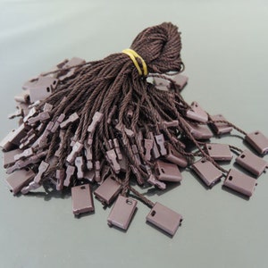 May include: A bundle of brown string tags with brown plastic loops. The tags are tied together with a rubber band.