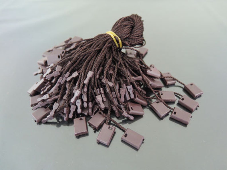 May include: A bundle of brown string tags with brown plastic loops. The tags are tied together with a rubber band.