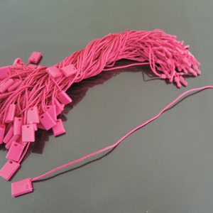 May include: A pile of pink string with small square tags attached to the ends. The string is bundled together and the tags are spread out.
