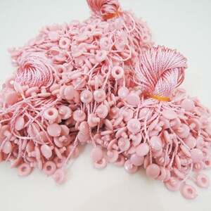 May include: A pile of pink string tags with small plastic buttons. The tags are used for attaching to clothing or other items.