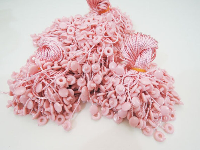 May include: A pile of pink string tags with small plastic buttons. The tags are used for attaching to clothing or other items.