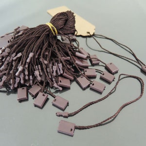 May include: A large pile of brown string tags with small brown plastic loops. The tags are tied together with a rubber band.