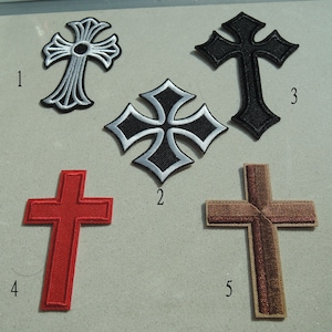 May include: Five different cross-shaped iron-on patches. The patches are in various colours and styles, including black, silver, red, and brown. The patches are numbered 1 through 5.