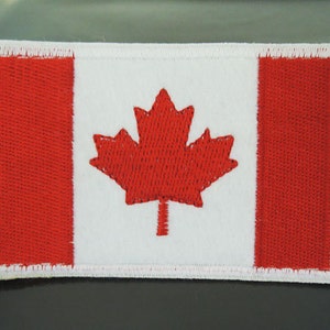 May include: A red and white embroidered Canadian flag patch. The flag features a red maple leaf on a white background with red stripes on either side.