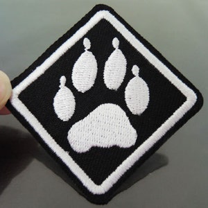 Op de afbeelding: Zwarte ruitvormige patch met een geborduurde witte poot.