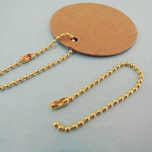 May include: Two gold ball chain keychains with a brown paper tag. The chains are about 6 inches long and have a lobster clasp.
