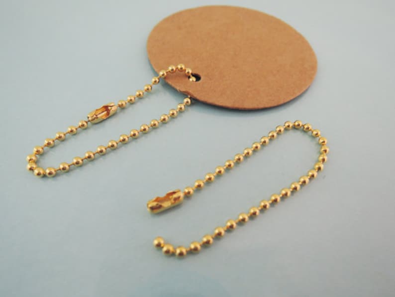 May include: Two gold ball chain keychains with a brown paper tag. The chains are about 6 inches long and have a lobster clasp.