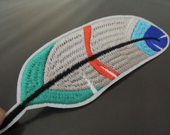 Puede incluir: Parche bordado con forma de pluma con cuerpo gris, borde verde azulado y detalles en rojo, azul y negro. El parche tiene un borde blanco. Este parche decorativo se puede planchar o coser en ropa o accesorios.