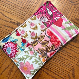 May include: A rectangular quilted fabric mat featuring a patchwork design of various floral and striped patterns in shades of hot pink, light pink, cream, green, and blue. The textile is stitched with a grid pattern and finished with piped edges.